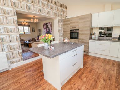 A kitchen with an island countertop and flowers on it next to a living room at Cushat House Stamford near Embleton