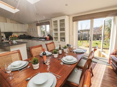 A dining room with a wooden table set for six and plants next to a kitchen and garden doors at Cushat House Stamford near Embleton