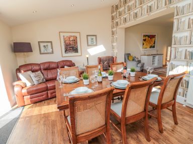 A dining area with a wooden dining table set with plates and glasses next to a brown leather sofa in a living room at Cushat House Stamford near Embleton