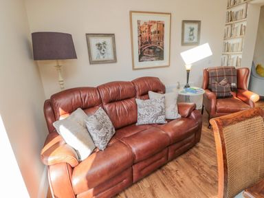 A living room with a brown leather sofa and armchair with cushions and framed pictures on the wall at Cushat House Stamford near Embleton