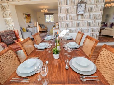 A dining table set with plates glasses and cutlery in a room with chairs and a wall with book patterned wallpaper at Cushat House Stamford near Embleton