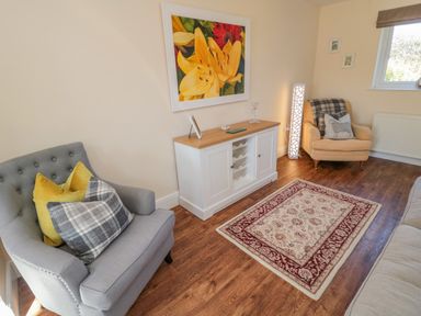 A sitting room with two armchairs a rug and a sideboard under a flower painting at Cushat House Stamford near Embleton