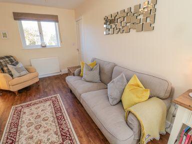 A sitting room with a grey sofa with cushions a yellow armchair and a patterned rug at Cushat House Stamford near Embleton