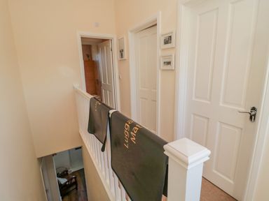 A hallway with white doors and white railing with black mats draped over the railing at Cushat House Stamford near Embleton