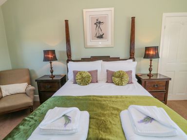 A bedroom with a four poster bed two bedside tables with lamps an armchair and folded towels on a green bedspread at Cushat House Stamford near Embleton