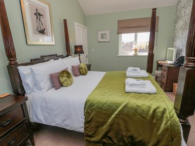 A bedroom with a four poster bed green blanket and bedside tables at Cushat House Stamford near Embleton