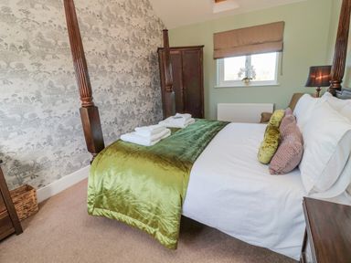 A bedroom with a four poster bed a green throw and folded towels at Cushat House Stamford near Embleton