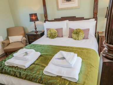 A bedroom with a large wooden bed with green and purple pillows bedside tables with lamps a chair and folded towels on the bed at Cushat House Stamford near Embleton