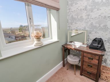 A corner with a window showing a candle on the sill and a wooden dressing table with a mirror stool and a hairdryer bag at Cushat House Stamford near Embleton