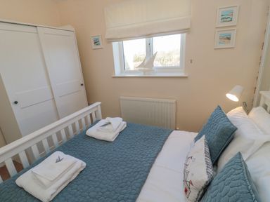 A bedroom with a bed with blue quilt and pillows two folded towels on bed a white wardrobe a window with a model sailboat on the sill and framed pictures on walls at Cushat House Stamford near Embleton
