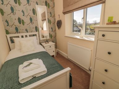 A small bedroom with a single bed bedside table with lamp tall mirror window with brown blind and a white chest of drawers at Cushat House Stamford near Embleton