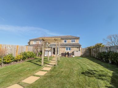 A backyard with a stone path, wooden pergola, and a stone house with a patio at Cushat House in Stamford near Embleton