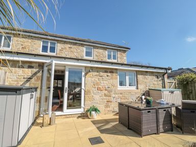 An outdoor patio with a glass door, a table with chairs, storage boxes, and a potted plant at Cushat House Stamford near Embleton