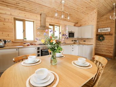 A kitchen with wooden walls a round dining table set with white dishes and a vase of flowers at The Larches in Van near Llanidloes