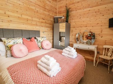 A bedroom with a bed with pillows and folded towels a wardrobe a vanity table with a mirror and flowers and a wooden chair at The Larches in Van near Llanidloes