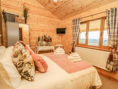 A bedroom with a bed pillows folded towels wardrobe vanity table chair window with curtains at The Larches in Van near Llanidloes