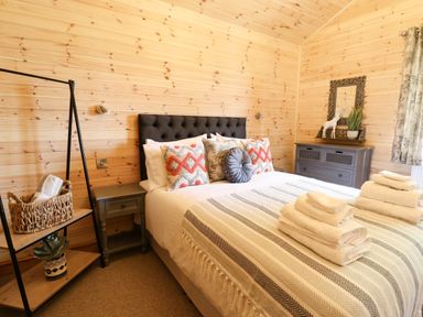 A bedroom with a bed with pillows and folded towels bedside tables a dresser with decorations and wooden walls at The Larches Van near Llanidloes