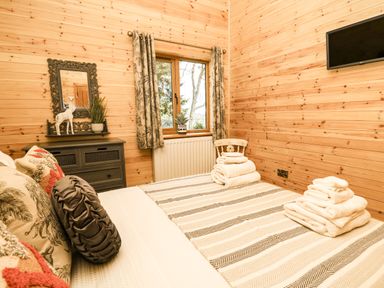 A bedroom with a bed, folded towels, a window with curtains, a mirror, and a television at The Larches in Van near Llanidloes