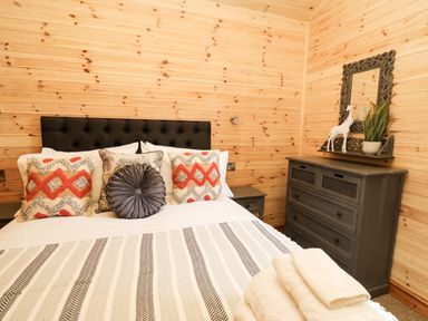 A bedroom with a bed pillows and blanket next to a wooden dresser with a mirror and decor at The Larches Van near Llanidloes