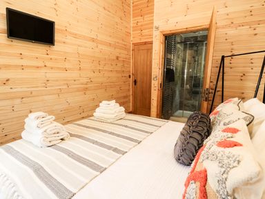 A bedroom with a striped bedspread folded towels and a wall-mounted television at The Larches Van near Llanidloes