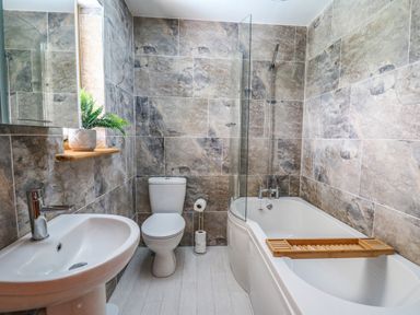 A bathroom with a sink a toilet a bathtub with a tray and a plant on a windowsill at The Larches in Van near Llanidloes