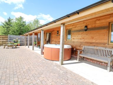 An outdoor patio with a covered wooden porch a hot tub a wooden bench and a picnic table with plants at The Larches in Van near Llanidloes