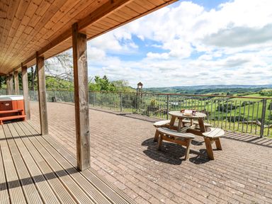 An outdoor covered patio with wooden columns a picnic table and a hot tub overlooking green hills at The Larches Van near Llanidloes