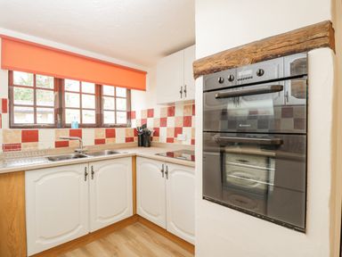 A kitchen with double oven built into the wall white cabinets a corner countertop and a window with orange blind at The Old Bakery in South Perrott near Mosterton
