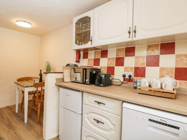 A kitchen with a small dining table and chairs a microwave and toaster on the countertop and a refrigerator and dishwasher below the counter at The Old Bakery in South Perrott near Mosterton