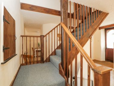 A stairway with blue carpet and wooden railing next to a wooden door and a small table in a hallway at The Old Bakery South Perrott near Mosterton