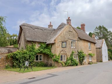 A stone cottage with a thatched roof and vegetation at The Old Bakery South Perrott near Mosterton