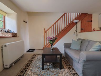 A living room with a sofa, coffee table, and staircase at Jasmine Cottage, South Perrott near Mosterton