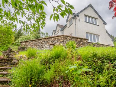 A stone house seen from a garden with stone steps and green plants at Hazelseat House in Graythwaite near Ulverston