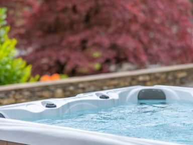 A hot tub with water and headrests near a stone wall and trees at Hazelseat House Graythwaite near Ulverston