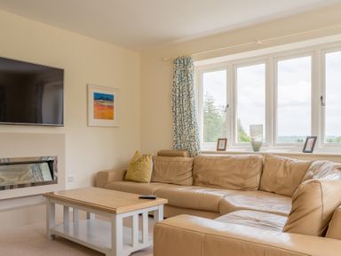 A living room with a leather sofa a wooden coffee table a wall-mounted tv and a window with curtains at Hazelseat House in Graythwaite near Ulverston