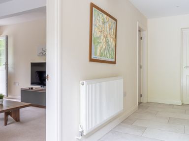 A hallway with a white radiator and a framed map on the wall next to a living room with a TV and a coffee table at Hazelseat House in Graythwaite near Ulverston