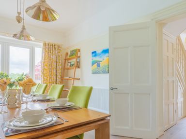 A dining room with a wooden table set with white dishes and green chairs near glass doors and a wooden ladder shelf at Hazelseat House in Graythwaite near Ulverston