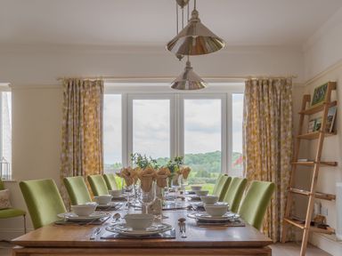 A dining room with a wooden table set with plates bowls and glasses and green chairs at Hazelseat House in Graythwaite near Ulverston