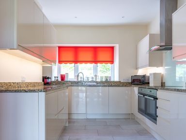 A kitchen with white cabinets granite countertops a double oven and a red window blind at Hazelseat House Graythwaite near Ulverston