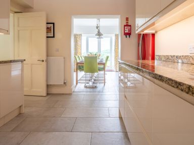 A kitchen area with a granite countertop and beige cabinets leading to a dining area with green chairs and a wooden table at Hazelseat House Graythwaite near Ulverston