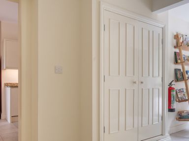 A hallway with double white doors a light switch and a wooden bookshelf with books and a fire extinguisher at Hazelseat House Graythwaite near Ulverston