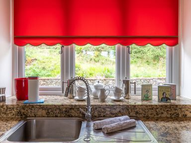 A kitchen sink with a flexible faucet and towels on the counter below a window with a red blind and various kitchen items on the windowsill at Hazelseat House in Graythwaite near Ulverston