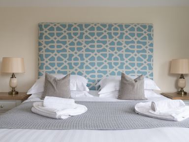 A bed with patterned headboard two pillows two bedside tables with lamps and folded towels at Hazelseat House in Graythwaite near Ulverston