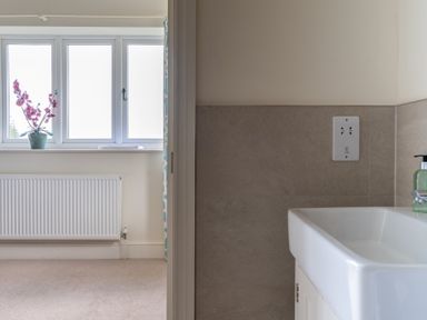 A bathroom sink with soap dispenser and a window with pink flowers on the sill at Hazelseat House in Graythwaite near Ulverston