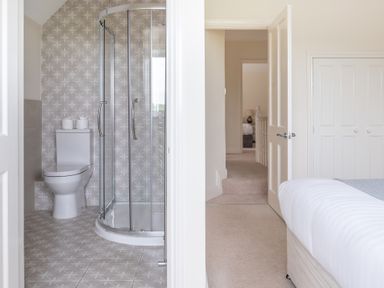 A bathroom with a toilet and glass shower next to a bedroom with a bed at Hazelseat House in Graythwaite near Ulverston
