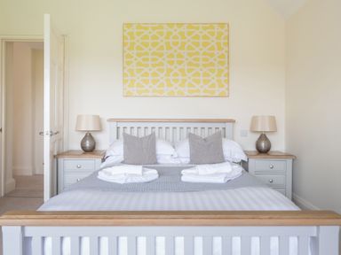 A bedroom with a double bed two bedside tables with lamps and a yellow patterned artwork at Hazelseat House in Graythwaite near Ulverston