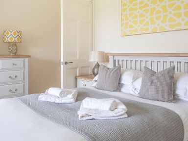 A bedroom with a double bed gray cushions and white towels on a grey blanket a bedside table with a lamp and a chest of drawers with a patterned lamp at Hazelseat House in Graythwaite near Ulverston
