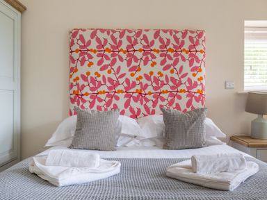 A bedroom with a bed with pink and orange leaf patterned headboard and gray pillows at Hazelseat House in Graythwaite near Ulverston