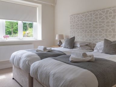 A bedroom with two single beds with grey blankets and pillows near a window with a white blind at Hazelseat House Graythwaite near Ulverston