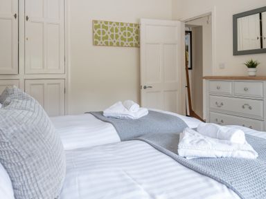 A bedroom with two beds and white towels on a grey runner a dresser with a mirror and a plant at Hazelseat House in Graythwaite near Ulverston